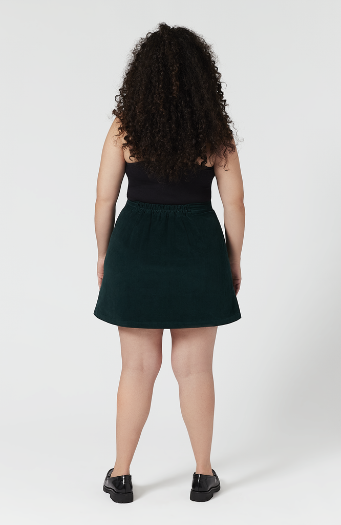 The Cord Mini skirt sits high at the waist with a roomy fit for full hips and thighs. Shown here is the back full view of the skirt in a deep, forest green shade.