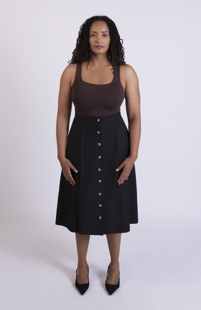The Wool Midi Skirt is a gorgeous A-line skirt that sits snug at the high waist with a loose, flowy drape through the seat, comfortably accommodating full hips and thighs. It has a center button closure and two thin pleats for movement. Shown here in a classic Black color.