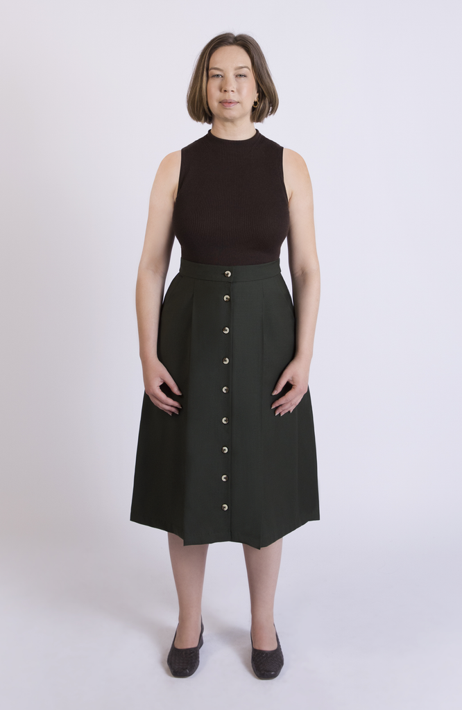 The Wool Midi Skirt is a gorgeous A-line skirt that sits snug at the high waist with a loose, flowy drape through the seat, comfortably accommodating full hips and thighs. It has a center button closure and two thin pleats for movement. Shown here in a gorgeous Green color.