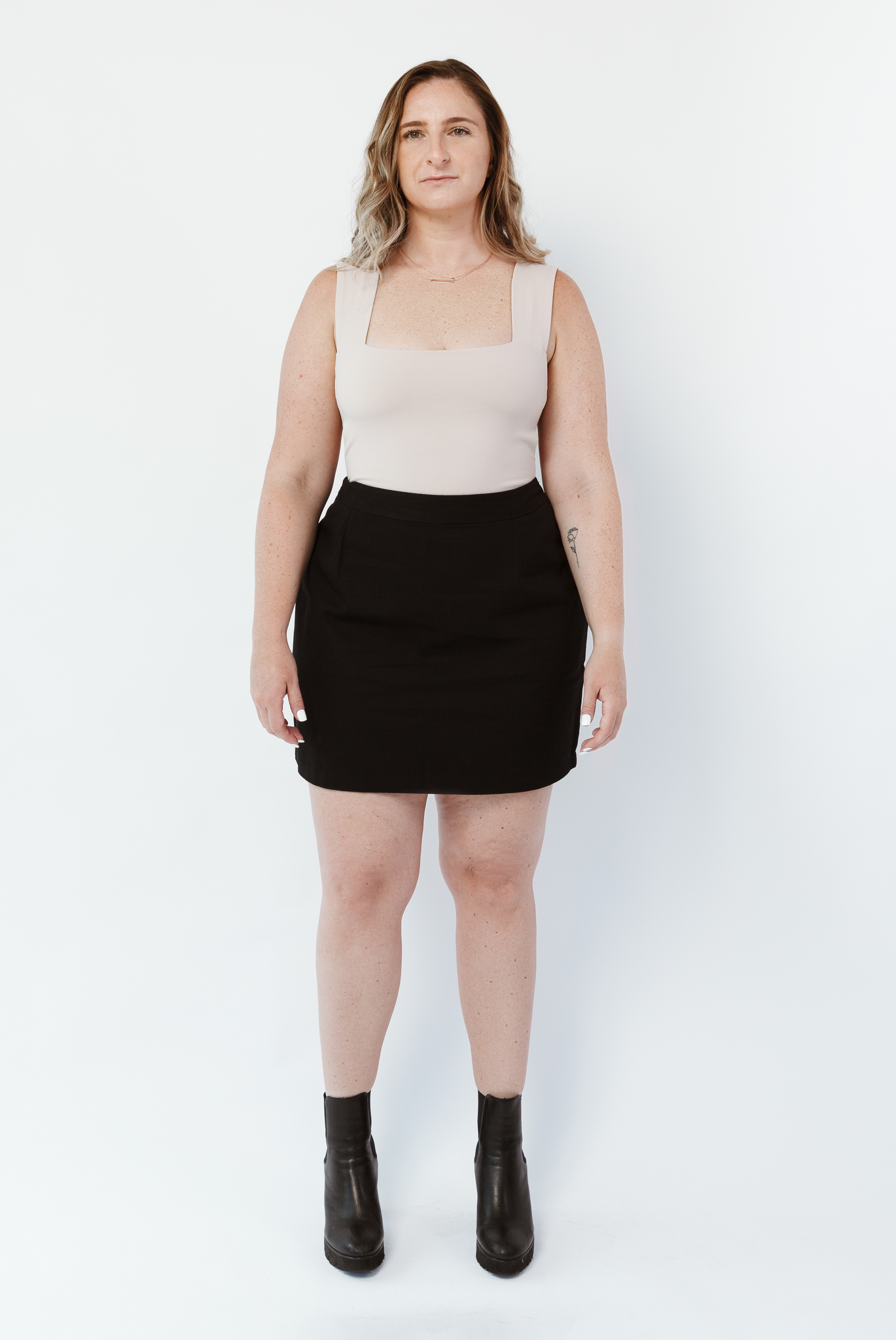 The Mini Skirt by Aam is designed for women with full hips and thighs. It's sit snug at the high waist with roomy fit through the seat for curvy bottom shapes. This image shows the front view of The Mini Skirt in black. It is shown on a model who is 5’5” and wearing a size Large. 