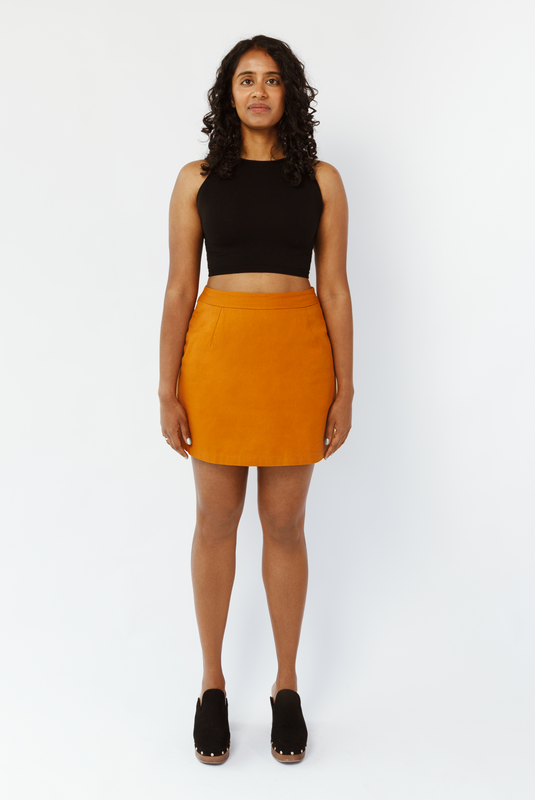 The Mini Skirt by Aam is designed for women with full hips and thighs. It's sit snug at the high waist with roomy fit through the seat for curvy bottom shapes. This image shows the front view of The Mini Skirt in Rust. It is shown on a model who is 5’7” and wearing a size Small.