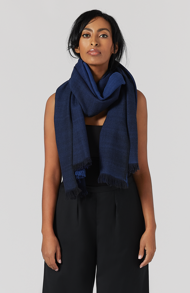 The Aurora Wrap by Aam The Label is a soft, warm 100% merino wool wrap that can be worn as a scarf or a shawl. It has been handwoven and is reversible. Here you can see the midnight color wrapped as a scarf.