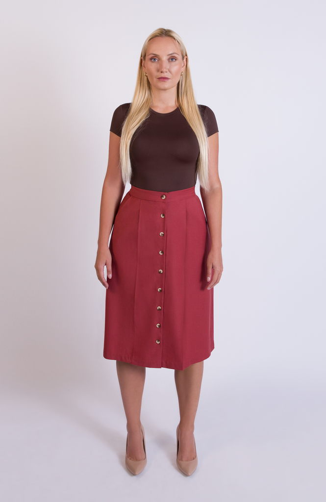 The Wool Midi Skirt is a gorgeous A-line skirt that sits snug at the high waist with a loose, flowy drape through the seat, comfortably accommodating full hips and thighs. It has a center button closure and two thin pleats for movement. Shown here in a gorgeous Deep Salmon pink color.
